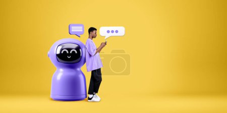 Photo for Black man typing in smartphone, standing full length near cartoon AI robot with speech bubbles on copy space empty yellow background. Concept of virtual assistant and chat bot - Royalty Free Image
