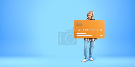 Téléchargez les photos : Femme hurlante tenant une carte de crédit maquillée, copier l'espace fond bleu vide. Concept de services bancaires en ligne, paiement d'argent, finances et achats - en image libre de droit