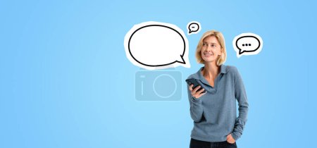 Photo for Smiling young woman using smartphone, mock up empty chat bubbles on copy space blue background. Concept of communication, social media and online network - Royalty Free Image