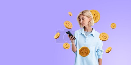 Téléchargez les photos : Jeune femme européenne tenant smartphone avec des pièces bigtcoin sur fond d'espace de copie violet. Concept de crypto-monnaie et d'exploitation minière - en image libre de droit