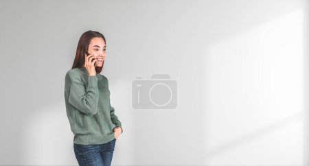 Foto de Retrato de la joven europea feliz hablando en el teléfono inteligente de pie cerca de la pared blanca. Concepto de comunicación y tecnología - Imagen libre de derechos