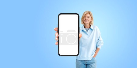 Foto de Mujer rubia feliz sonriendo, mostrando un gran teléfono inteligente simulan pantalla de espacio de copia sobre fondo azul. Concepto de redes sociales, aplicación móvil, sitio web y compras en línea - Imagen libre de derechos