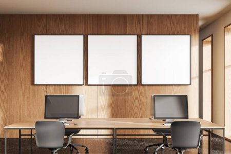 Photo for Wooden coworking interior with chairs, table with pc monitors in row. Cozy workspace with panoramic window. Three mock up canvas posters in row. 3D rendering - Royalty Free Image