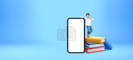 Photo for Cheerful little boy standing on stack of books near big smartphone with mock up display and showing thumb up gesture. Concept of digital library and e-learning - Royalty Free Image