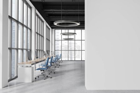 Foto de Interior de la moderna oficina de espacio abierto con paredes blancas, suelo de hormigón y fila de mesas de ordenador con sillas azules de pie cerca de la ventana panorámica. Copia la pared del espacio a la derecha. renderizado 3d - Imagen libre de derechos