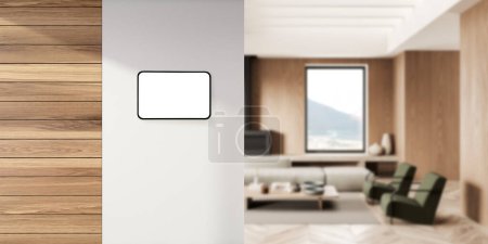 Téléchargez les photos : Vue de la tablette moderne maison intelligente suspendue au mur dans le salon flou avec fauteuils confortables et table basse. Rendu 3d - en image libre de droit