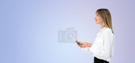 Téléchargez les photos : Vue latérale de belle jeune femme européenne à l'aide d'un ordinateur tablette debout sur fond d'espace de copie violet. Concept de médias sociaux et de communication - en image libre de droit