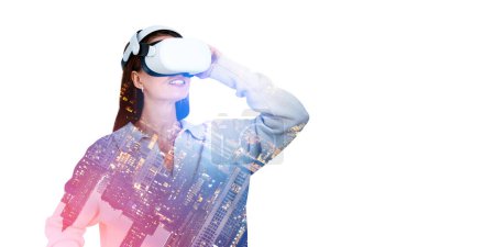 Téléchargez les photos : Jeune femme européenne utilisant des lunettes VR avec double exposition de paysage urbain sur fond blanc. Concept de métaverse et de cyberespace - en image libre de droit