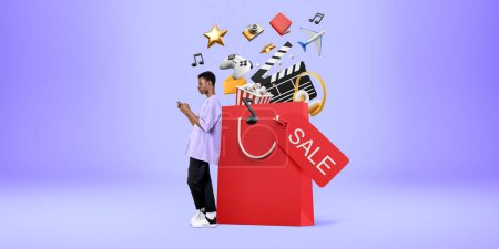 Photo for Young African Amreican man with smartphone standing near big shopping bag with online shopping icons over purple background. Concept of e-commerce and money transaction - Royalty Free Image