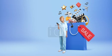 Photo for Young European woman with smartphone standing near big shopping bag with online shopping icons over blue background. Concept of e-commerce and money transaction - Royalty Free Image