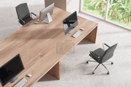 Foto de Vista superior del interior moderno coworking con escritorio pc en mesa compartida, piso de hormigón ligero. Elegante rincón de trabajo con muebles minimalistas y ventana panorámica en los trópicos. Renderizado 3D - Imagen libre de derechos