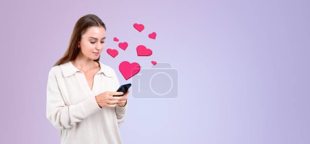 Téléchargez les photos : Portrait d'une jeune femme européenne joyeuse utilisant un smartphone avec des médias sociaux et des icônes de cœur sur fond d'espace de copie violet. Concept de communication en ligne - en image libre de droit