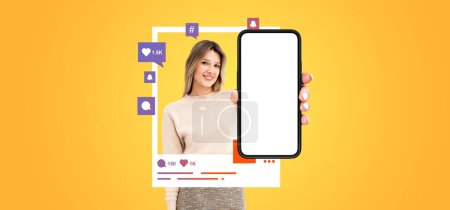 Foto de Joven mujer europea alegre mostrando teléfono inteligente con pantalla simulada y los iconos de las redes sociales alrededor de ella de pie sobre el fondo amarillo. Concepto de comunicación online - Imagen libre de derechos