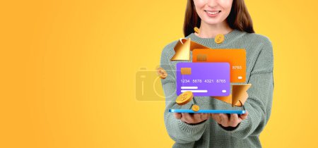 Foto de Mujer sonriente, manos sosteniendo la tableta y dos maquetas de tarjetas de crédito y flecha, fondo de color vacío. Concepto de transferencia de dinero, cuenta bancaria y servicio móvil - Imagen libre de derechos