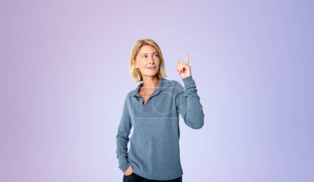Photo for Portrait of happy young European woman pointing upwards with index finger standing over purple background. Concept of planning and bright idea - Royalty Free Image