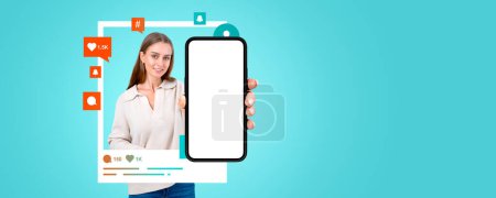 Happy young European woman showing smartphone with mock up screen and social media icons around her standing over green copy space background. Online communication concept