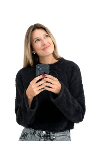 Foto de Sonriente mujer joven soñando usando teléfono, retrato mirando hacia arriba aislado sobre fondo blanco. Concepto de comunicación en línea, compras, redes y redes sociales - Imagen libre de derechos