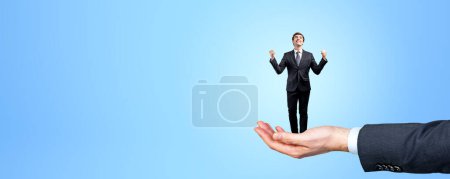 Photo for Man hand holding a businessman with raised hands, happy employee celebrating promotion or recruitment on copy space empty blue background. Concept of career and human resources - Royalty Free Image