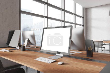 Téléchargez les photos : Vue en angle de l'intérieur du lieu de travail avec écran blanc d'ordinateur PC maquette, zone de coworking avec des tables en rangée. Fenêtre panoramique sur les gratte-ciel de Singapour. rendu 3D - en image libre de droit