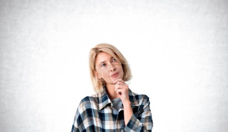 Photo for Young European woman wearing checkered shirt and thinking with finger on chin choosing her way in life and career path. Concept of brainstorming and information processing. Choice and pondering - Royalty Free Image