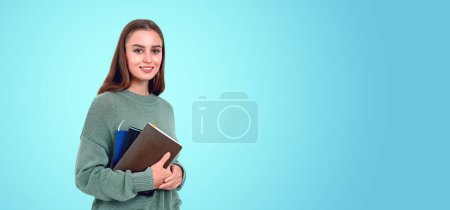 Téléchargez les photos : Une femme souriante tenant des livres sur fond de sarcelle, représentant l'éducation avec amplement d'espace de copie - en image libre de droit
