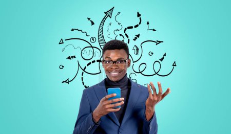 Foto de Hombre de negocios negro sonriente usando el teléfono haciendo un gesto amistoso, flechas negras y líneas de garabatos moviéndose en diferentes direcciones. Concepto de buena elección, ayuda, comunicación y desarrollo - Imagen libre de derechos