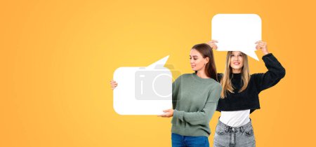 Photo for Two smiling beautiful women showing mock up blank clouds, copy space orange background. Concept of recommendation, opinion, teamwork, conference or student team - Royalty Free Image