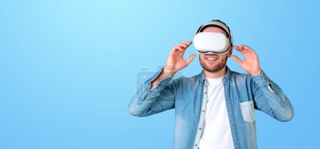 Foto de Un hombre con un casco VR, ajustándolo con las manos, sobre un fondo azul claro, concepto de realidad virtual - Imagen libre de derechos