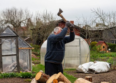 Ein Mann arbeitet mit einer Axt in seinem Hof, verarbeitet Brennholz für die Wintersaison, verbrennt Brennholz, heizt Brennholz auf dem Land