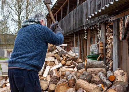 A man works with an ax in his yard, processing firewood for the winter season, burning firewood, heating firewood in the countryside
