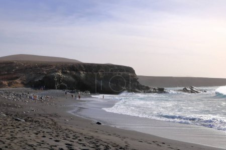 November 20 2023 - Ajuy, Fuerteventura in Spain: people enjoy the beach, made up of black volcanic sand and stones