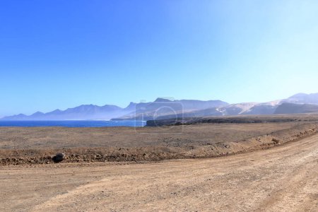 Carretera de grava, polvorienta con altas montañas volcánicas al fondo. Jandia, Morro Jable, Fuerteventura, Islas Canarias en España