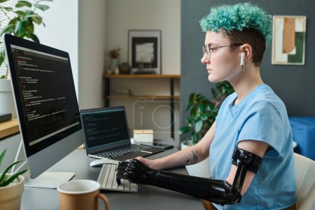 Téléchargez les photos : Jeune spécialiste informatique avec bras prothétique se concentrant sur son travail en ligne, elle travaille avec des codes de sécurité - en image libre de droit
