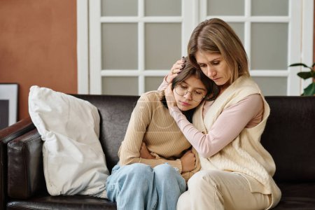 Photo for Mother sitting on sofa together with her daughter and embracing her, she comforting her during depression - Royalty Free Image