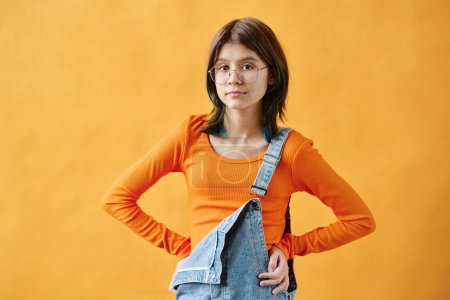 Téléchargez les photos : Portrait d'adolescente en chemise orange regardant la caméra debout sur fond orange - en image libre de droit