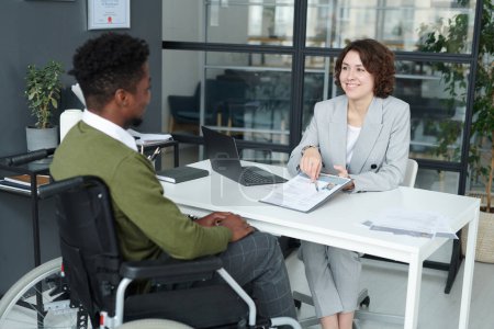Photo for Young manager pointing at resume and discussing it together with candidate with disability during meeting - Royalty Free Image