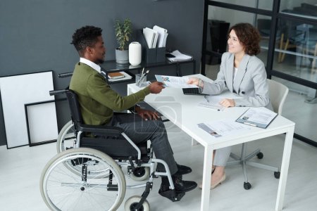 Photo for High angle view of businesswoman having job interview with man with disability while they sitting at table in modern office - Royalty Free Image