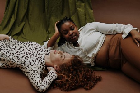Photo for Portrait of two women of different types relaxing on floor against the green and brown background - Royalty Free Image