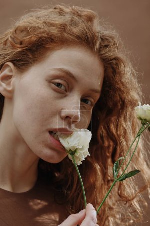 Portrait of ginger girl with natural beauty looking at camera and biting white flower