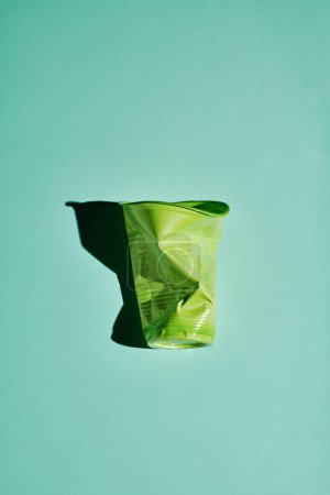Photo for Vertical modern flat lay shot of crumpled green plastic cup on light bluish green background, conscious consumption and recycling concept - Royalty Free Image