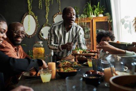 Afrikanischer reifer Mann schlägt Gericht für seine Familie vor, während sie am Tisch im Esszimmer sitzen