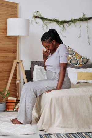 Téléchargez les photos : Africaine assise sur le canapé et se sentant malade pendant sa grossesse - en image libre de droit
