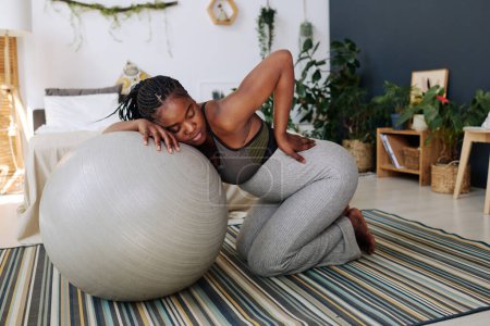 Photo for African pregnant girl in pain leaning on fitness ball with her eyes closed during labor in room - Royalty Free Image