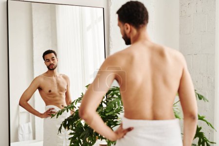 Rear view of young shirtless man looking at his muscular body in mirror