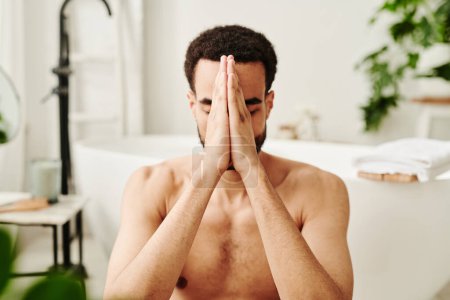 Téléchargez les photos : Jeune homme torse nu tenant ses mains devant son visage et méditant les yeux fermés le matin - en image libre de droit