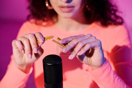 Selektive Fouc-Nahaufnahme einer jungen weiblichen Influencerin, die im Studio in rosa Neonlicht sitzt und knackige Buiscuit-Sticks aufnimmt, die Sounds für ASMR-Vlog brechen