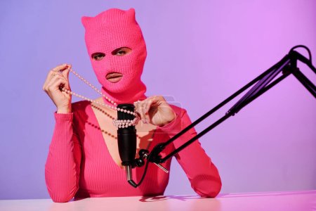 Unrecognizable young female influencer wearing pink sweater and balaclava recording ASMR content using bead necklace