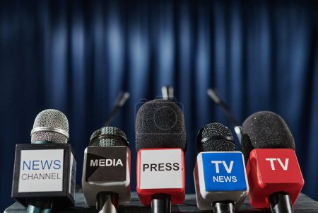 Foto de Primer plano de micrófonos de diferentes medios de televisión frente a tribuna para altavoz en conferencia de prensa - Imagen libre de derechos