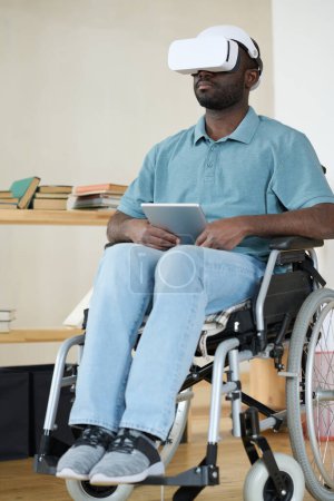 Photo for African AMerican man in VR goggles sitting in wheelchair using digital tablet for virtual reality therapy - Royalty Free Image