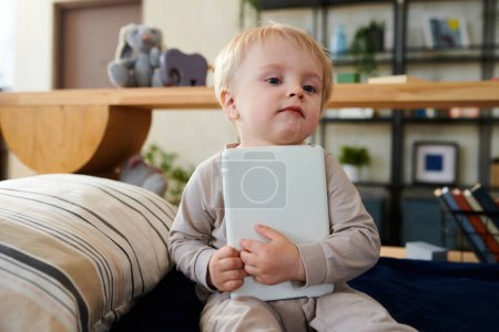 Photo for Cute little child sitting on bed with digital tablet and playng with it at home - Royalty Free Image